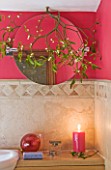 RICKYARD BARN HOUSE  OXFORDSHIRE: DESIGNERS JANE AND CLIVE NICHOLS. BATHROOM WITH TILES  PINK/ RED PAINTED WALL  SINK  CANDLE AND MISTLETOE AROUND CIRCULAR MIRROR - CHRISTMAS