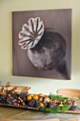 RICKYARD BARN HOUSE  OXFORDSHIRE: DESIGNERS JANE AND CLIVE NICHOLS. SEPIA TONE PHOTO CANVAS OF POPPY SEED HEAD BY CLIVE NICHOLS ON KITCHEN WALL WITH DRIED FRUIT DISPLAY ON TABLE