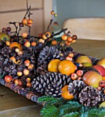 RICKYARD BARN HOUSE  OXFORDSHIRE: DESIGNERS JANE AND CLIVE NICHOLS. CHRISTMAS DECORATION ON TABLE - WICKER LEAF WITH FIR CONES  FRUIT AND BERRIES