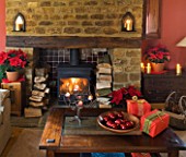 RICKYARD BARN HOUSE  OXFORDSHIRE: DESIGNERS JANE AND CLIVE NICHOLS. LIVING ROOM AT CHRISTMAS WITH WRAPPED PRESENTS  POINSETTIAS IN CONTAINERS AND WOOD BURNING FIRE