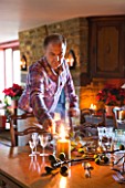 RICKYARD BARN  OXFORDSHIRE: CHRISTMAS - LIVING ROOM - CLIVE NICHOLS LIGHTS CANDLE ON THE DINING TABLE DECORATED WITH CANDLES  FIGS AND FIG LEAVES CUT FROM THE GARDEN