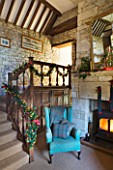 FULBROOK HOUSE: GALLERIED MAIN HALL WITH COTSWOLD STONE FIREPLACE  LOG BURNING STOVE AND LEATHER AND UPHOLSTERED ARMCHAIRS WITH CHRISTMAS TREE REFLECTED IN LARGE MIRROR.