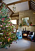 FULBROOK HOUSE: GALLERIED MAIN HALL WITH COTSWOLD STONE FIREPLACE  LOG BURNING STOVE  MIRROR AND LEATHER AND UPHOLSTERED ARMCHAIRS WITH CHRISTMAS TREE