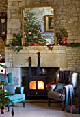 FULBROOK HOUSE: GALLERIED MAIN HALL WITH COTSWOLD STONE FIREPLACE  LOG BURNING STOVE  CHRISTMAS TREE REFLECTED IN MIRROR AND LEATHER AND UPHOLSTERED ARMCHAIRS