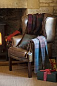 FULBROOK HOUSE: GALLERIED MAIN HALL WITH COTSWOLD STONE FIREPLACE AND LEATHER ARMCHAIR WITH CHRISTMAS PRESENTS