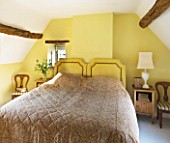 FULBROOK HOUSE: YELLOW DOUBLE BEDROOM WITH EAVED CEILING AND BEAMS. ANTIQUE POLISHED WOOD CHAIR WITH GOLD AND GREEN STRIPE FABRIC SEAT WITH OLD BOOKS