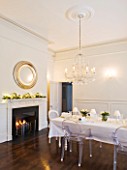 WHITE HOUSE: WHITE DINING ROOM WITH CENTRAL GLASS CHANDELIER AND SILVER ROUND MIRROR ABOVE MANTEL PIECE. LONG DINING TABLE DRESSED IN WHITE LINEN WITH TRANSPARENT GHOST CHAIRS