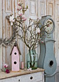 PETERSHAM NURSERIES  RICHMOND  SURREY: DRESSER WITH MAGNOLIA IN GLASS CONTAINER WITH BIRD HOUSE AND BLUE CLOCK