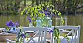 FISHING COTTAGE  KNEBWORTH PARK: STYLING BY JACKY HOBBS: TABLE AND CHAIRS ON JETTY BESIDE LAKE  WITH BLUEBELLS IN VARIOUS GLASS JARS AND CONTAINERS - SPRING