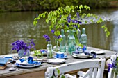 FISHING COTTAGE  KNEBWORTH PARK: STYLING BY JACKY HOBBS: TABLE AND CHAIRS ON JETTY BESIDE LAKE  WITH TABLE SETTING WITH BLUEBELLS IN VARIOUS GLASS JARS AND CONTAINERS -SPRING