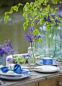 FISHING COTTAGE  KNEBWORTH PARK: STYLING BY JACKY HOBBS: TABLE ON JETTY BESIDE LAKE  WITH TABLE SETTING WITH BLUEBELLS IN VARIOUS GLASS JARS AND CONTAINERS -SPRING