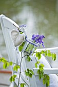 FISHING COTTAGE  KNEBWORTH PARK: STYLING BY JACKY HOBBS: WHITE WOODEN CHAIR BESIDE WITH GLASS FILLED WITH BLUEBELLS AND SPING FOLIAGE HANGING FROM BACK OF CHAIR