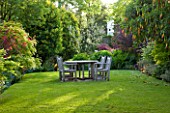 GRANGE COURT  GUERNSEY: WOODEN TABLE AND CHAIRS ON THE LAWN WITH BRUGMANSIA SANGUINEA IN FLOWER ON THE RIGHT