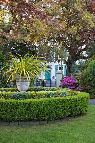 GRANGE_COURT__GUERNSEY_VIEW_TO_COLONIAL_STYLE_HOUSE_WITH_BOX_CIRCLES_AND_URN_PLANTED_WITH_PHORMIUM