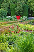 CHATEAU DU RIVAU  LOIRE VALLEY  FRANCE: PEACOCK IN THE FAIRIES BORDER WITH IMPERATA CYLINDRICA RED BARON AND RED OVERSWCALED CONTAINER - RED POT BY JEAN-PIERRE RAYNAUD
