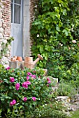 LES JARDINS DE ROQUELIN  LOIRE VALLEY  FRANCE: A VINTAGE WATERING CAN ON THE15TH CENTURY FARMHOUSE STEPS WITH ROSE ROSERAIE DE LHAY
