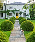 GIPSY HOUSE  BUCKINGHAMSHIRE: THE FRONT GARDEN WITH STONE PATH  HOUSE WITH YELLOW DOOR  CLIPPED YEW TOPIARY BALLS AND PESTO THE DOG
