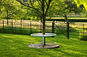 GIPSY HOUSE  BUCKINGHAMSHIRE: METAL TREE SEAT ON LAWN WITH THE MEADOW BEHIND