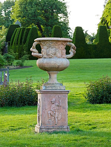 NYMANS__SUSSEX_THE_NATIONAL_TRUST_URN_ON_MAIN_LAWN_WITH_TOPIARY_YEW_HEDGING_BEHIND__EVENING_LIGHT__J