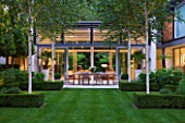 THE GLASS HOUSE  PETERSHAM. ARCHITECTS TERRY FARRELL PARTNERS. GARDEN DESIGN BY SALLIS CHANDLER: NIGHT VIEW OF LAWN  GLASS PAVILION  BETULA JACQUEMONTII AND HYDRANGEA ANNABELLE