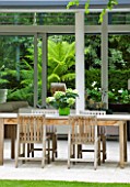 THE GLASS HOUSE  PETERSHAM. ARCHITECTS TERRY FARRELL PARTNERS. GARDEN DESIGN BY SALLIS CHANDLER: LIMESTONE PATIO  TABLE AND CHAIRS  VIEW THROUGH GLASS PAVILION TO TREE FERN GARDEN