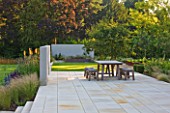 DEW POND HOUSE: DESIGN BY WILSON MCWILLIAM STUDIO - MAIN TERRACE/PATIO - TABLE & CHAIRS  AMELANCHIER LAMARCKII  IPE DECKING  PALE SANDSTONE PAVING. STIPA  KNIPHOFIA TAWNY KING