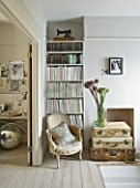 TWIG HUTCHINSON HOUSE  LONDON: WHITE LIVING ROOM WITH CHAIR  BOOKCASE  ALLIUMS IN GLASS JAR WITH SUITCASES BENEATH
