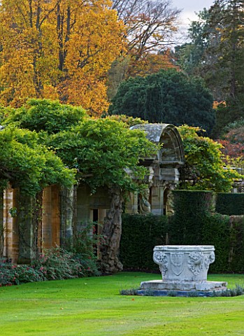 HEVER_CASTLE__KENT_AUTUMN_LARGE_URN_CONTAINER_IN_LAWN_WITH_AUTUMN_COLOUR_IN_THE_ITALIAN_GARDENS