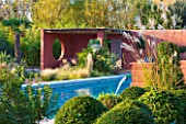 AFRICAN GARDEN  PROVENCE  FRANCE: DESIGNER DOMINIQUE LAFOURCADE: SWIMMING POOL WITH TERRACOTTA-TONED STUCCO WALLS OF THE PATIO BEHIND