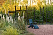 AFRICAN GARDEN  PROVENCE  FRANCE: DESIGNER DOMINIQUE LAFOURCADE: PAMPAS GRASS AND BLACKENED WOOD FENCING WITH BLACK LOUNGER/ SEAT ON ROSE COLOURED GRAVEL