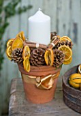 THE GARDEN AND PLANT COMPANY  HATHEROP  GLOUCESTERSHIRE: PLANT POT CANDLE TABLE  CENTREPIECE DECORATED WITH PINE CONES  DRIED ORANGE SLICES AND CINNAMON STICKS