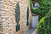 GARDEN IN LUBERON  FRANCE  DESIGNED BY MICHEL SEMINI: WOODEN TROMPE LOEIL TREES IN CONTAINERS ON WALL BESIDE THE BACK DOOR