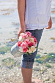 THE ISLES OF SCILLY: SCILLY FLOWERS - FRESHLY PICKED SCENTED PINKS IN METAL JUG BY SEA  HELD BY STEPH HILL