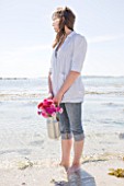 THE ISLES OF SCILLY: SCILLY FLOWERS - FRESHLY PICKED SCENTED PINKS IN METAL JUG BY SEA  HELD BY STEPH HILL