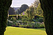 GLYNDEBOURNE, EAST SUSSEX: VIEW THROUGH YEW TREES TO LAWN AND BORDER WITH EREMURUS, ALLIUMS AND BERBERIS - BEYOND IS THE CHAMPAGNE TENT