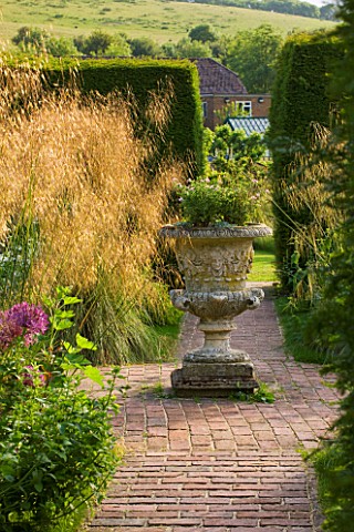 GLYNDEBOURNE_EAST_SUSSEX_VIEW_ALONG_BRICK_PATH_TO_STONE_URN_AND_GAP_THROUGH_YEW_HEDGES__STIPA_GIGANT