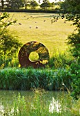 GARDEN IN KENT DESIGNED BY BELLA WHITELEY: THE PORTAL SCULPTURE BY DAVID HARBER BESIDE THE POOL, POND, LAKE. ORNAMENT, REFLECTION, REFLECTED, REFLECTIONS. BORROWED LANDSCAPE