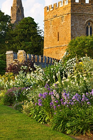 BROUGHTON_CASTLE_OXFORDSHIRE_HERBACEOUS_BORDER_ALONG_THE_GARDEN_WALL_WITH_THE_GATEHOUSE_AND_CHURCH_B