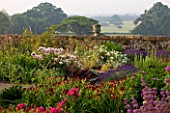 KILLERTON  DEVON: THE NATIONAL TRUST- HERBACEOUS GARDEN WITH ROSES  LAVENDER AND HEMEROCALLIS - URN AND PARKLAND BEYOND