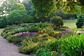 KILLERTON  DEVON: THE NATIONAL TRUST- HERBACEOUS GARDEN WITH LAWN AND WOODLAND BEYOND - EVENING LIGHT