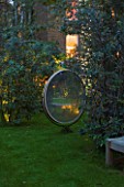 NOTTING HILL HOUSE, LONDON. GARDEN DESIGN BY BUTTER WAKEFIELD.ANTIQUE MIRROR AS FEATURE ON LAWN WITH TREE ADORNED WITH FAIRY LIGHTS. NIGHT,LIT,LIGHTING,EVENING,DUSK,GLOW,REFLECTION