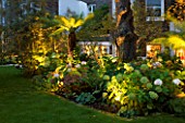 NOTTING HILL HOUSE, LONDON. GARDEN DESIGN BY BUTTER WAKEFIELD. BORDER LIT UP AT NIGHT WITH HYDRANGEAS AND TREE FERNS. UPLIGHTING,LIGHT,EVENING,DUSK,GLOW