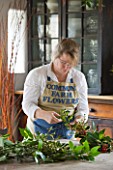COMMON FARM FLOWERS. SOMERSET: GEORGIE NEWBERY  FOUNDER AND OWNER OF COMMON FARM FLOWERS  MAKES A BRITISH GROWN SEASONAL FOLIAGE GARLAND WITH LAUREL  HOLLY AND VIBURNUM DAVIDII