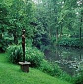 EVE BY MARZIA COLONNA STANDS BESIDE THE LAKE IN THE HANNAH PESCHAR GALLERY GARDEN  SURREY