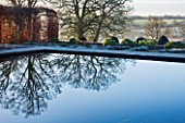 BROUGHTON GRANGE, OXFORDSHIRE: DESIGNER TOM STUART - SMITH: BEECH HEDGES IN FROST IN THE WALLED GARDEN WITH REFLECTIONS ON WATER. WINTER, COUNTRY GARDEN, TRIMMED, POOL, LAKE, POND