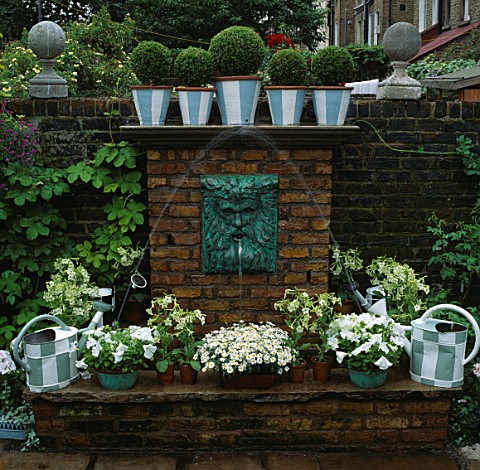 WATER_FEATURE_WALL_MOUNTED_HEAD_OF_NEPTUNE_WATER_SPOUT_ABOVE_BRICK_POOL_PAINTED_WATERING_CANS__CONTA