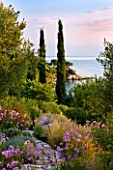 CORFU, GREECE - THE KASSIOPIA ESTATE: VIEW OUT TO SEA FROM GARDEN WITH STONE PATH,  STIPA TENUISSUIMA, TULBAGHIA VIOLACEA AND CYPRESS TREES