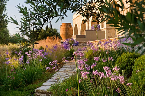 CORFU_GREECE__THE_KASSIOPIA_ESTATE_VIEW_LOOKING_UP_TOWARDS_VILLA_WITH_STONE_URN_PATH_AND_PINK_FLOWER