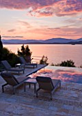 CORFU, GREECE - THE KASSIOPIA ESTATE: EVENING LIGHT - DUSK ON THE TERRACE LOOKING OUT TO SEA WITH SUN LOUNGERS. IN THE DISTANCE ARE THE ALBANIAN MOUNTAINS