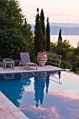 CORFU, GREECE - THE KASSIOPIA ESTATE: THE SWIMMING POOL WITH SUN LOUNGER AND TERRACOTTA ON THE TERRACE WITH CYPRESS TREES. REFLECTION.